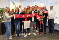Die besonderen Lätzchen hat Fabian Pesch, Mitgliedermanger des 1. FC Köln (5.v.r.) überreicht an Bürgermeister Mario Dahm (4.v.R.) sowie die Ehrenamtlichen Lissy Wedding (2.v.l.) und Assunta Schlüter (3.v.l.), NBD-Leiterin Anna Klein (3.v.r.), den Malteser-Ortsbeauftragten Hans Schramm (2.v.r.) sowie den Beigeordneten Martin Herkt (4.v.l.) und Miriam Overath (5.v.l.), Leiterin des Amtes für Kinder, Jugend und Familie der Stadt Hennef.